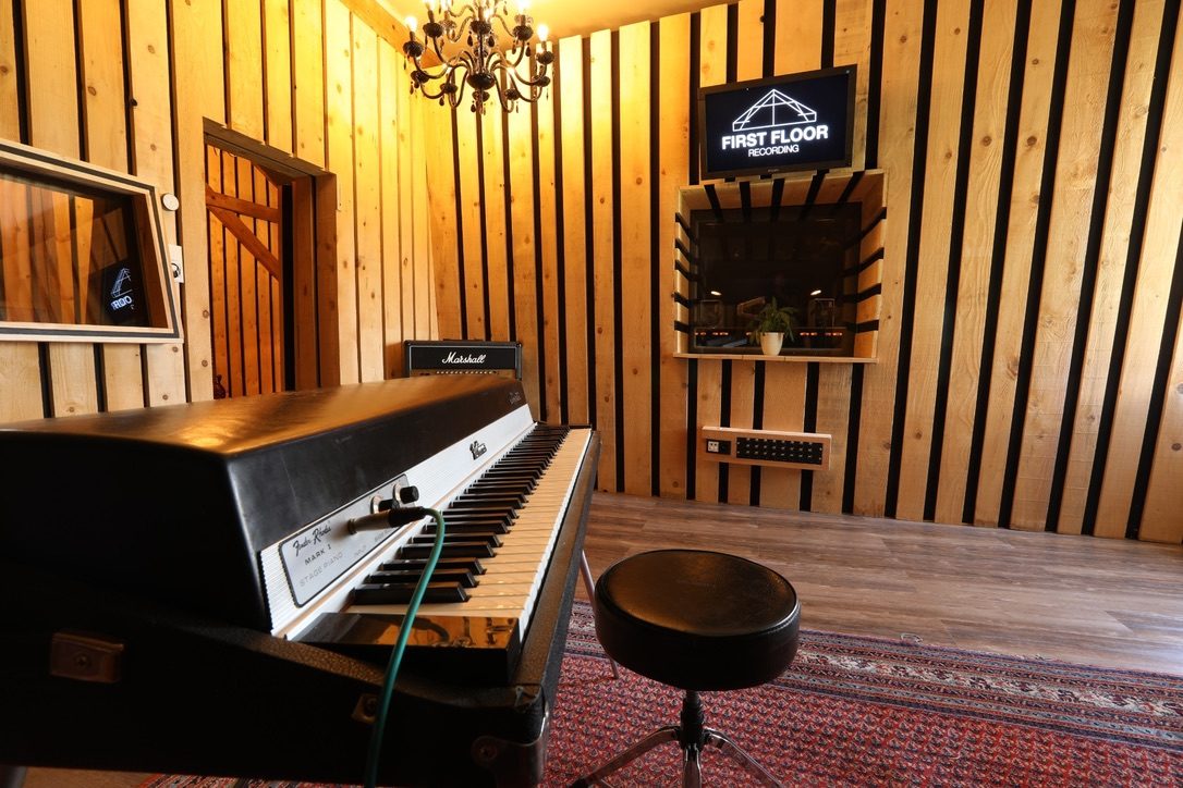 Pièce de studio avec piano, bois mural et logo First Floor Recording