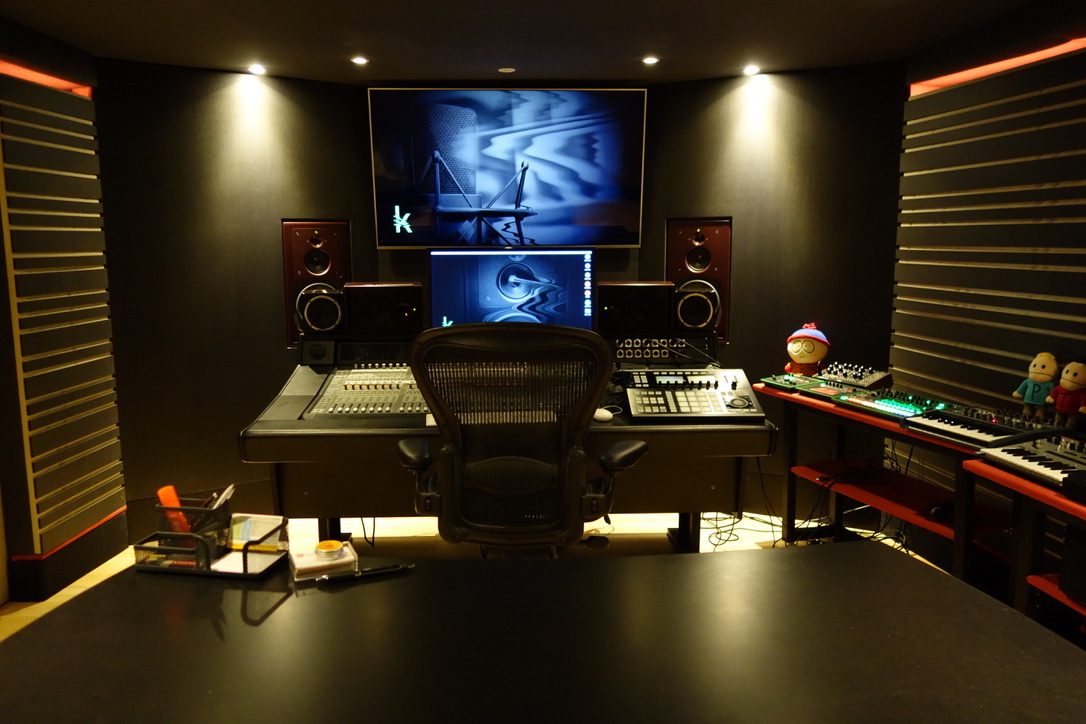 Régie sombre avec grand écran, console audio, enceintes et claviers