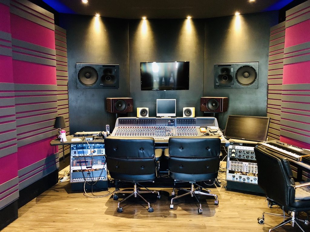Régie studio avec console audio, enceintes encastrées et panneaux acoustiques roses